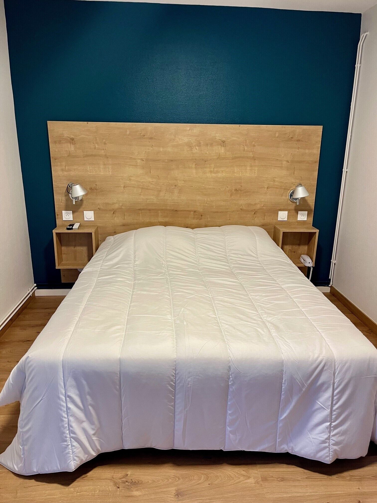 Una cama con cabecera de madera, dos mesitas de noche con lámparas y una pared azul decorativa.