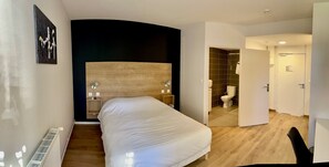 Un dormitorio moderno con una cama grande, cabecera de madera, mesita de noche y lámpara de pared.