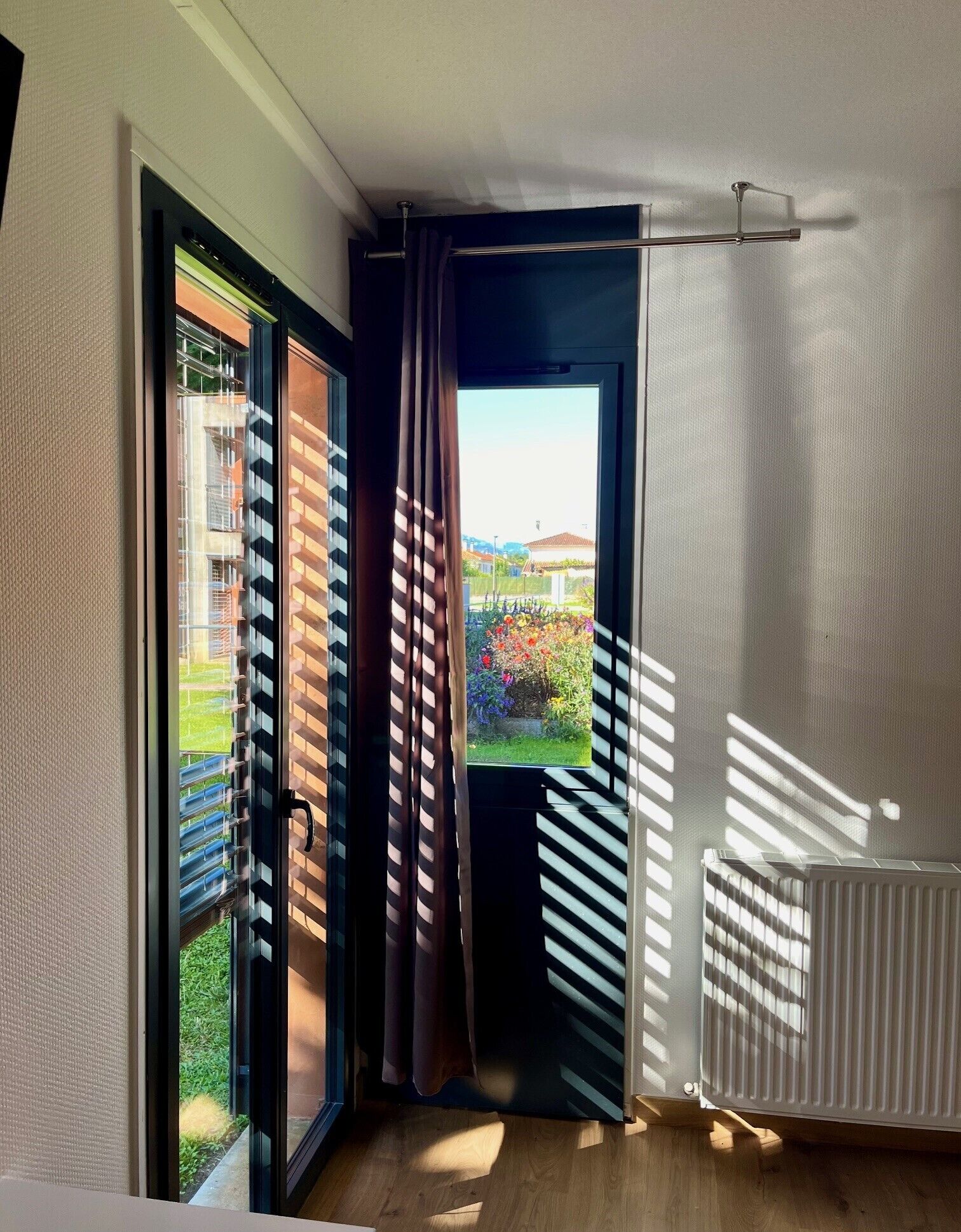 Una habitación con puerta de cristal corredera que da a un balcón, un radiador y vistas a una zona residencial.