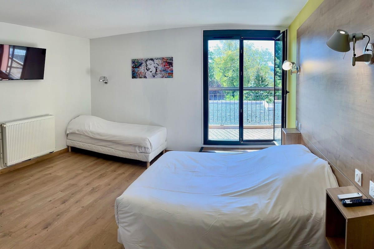 Ein Schlafzimmer mit Bett, einer kleinen Couch, einem Fernseher, einer Heizung, einem Gemälde und einem Balkon mit Blick.
