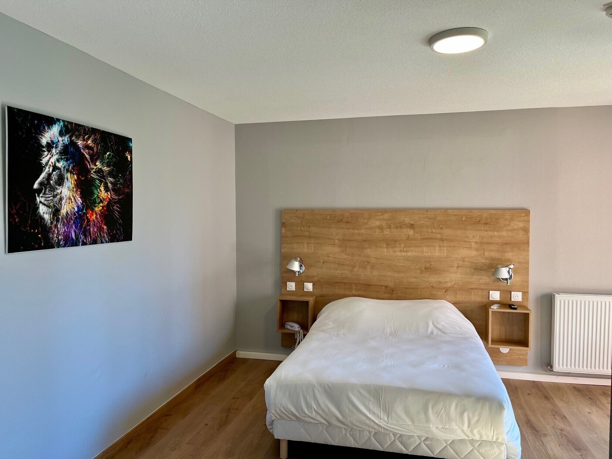 Un dormitorio con cabecera de madera, una cama con ropa blanca, dos mesitas de noche con lámparas y un cuadro colgado en la pared.