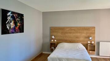 Un dormitorio con cabecera de madera, una cama con ropa blanca, dos mesitas de noche con lámparas y un cuadro colgado en la pared.