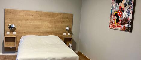 Un dormitorio con cabecera de madera, cama con ropa de cama blanca, dos mesitas de noche con lámparas y un cuadro abstracto colorido en la pared.