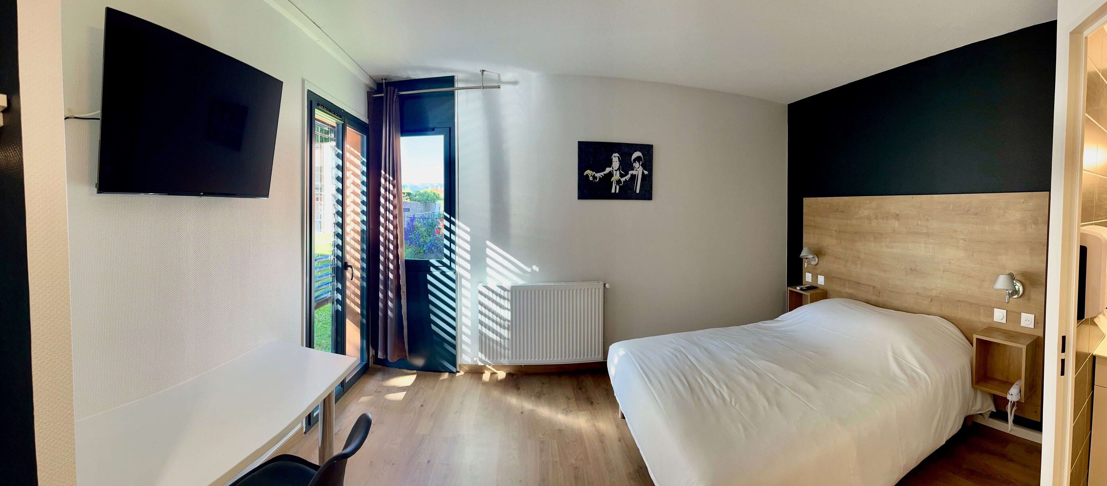 Un dormitorio con una cama, un escritorio, una silla, un televisor, un radiador y una ventana con cortinas.