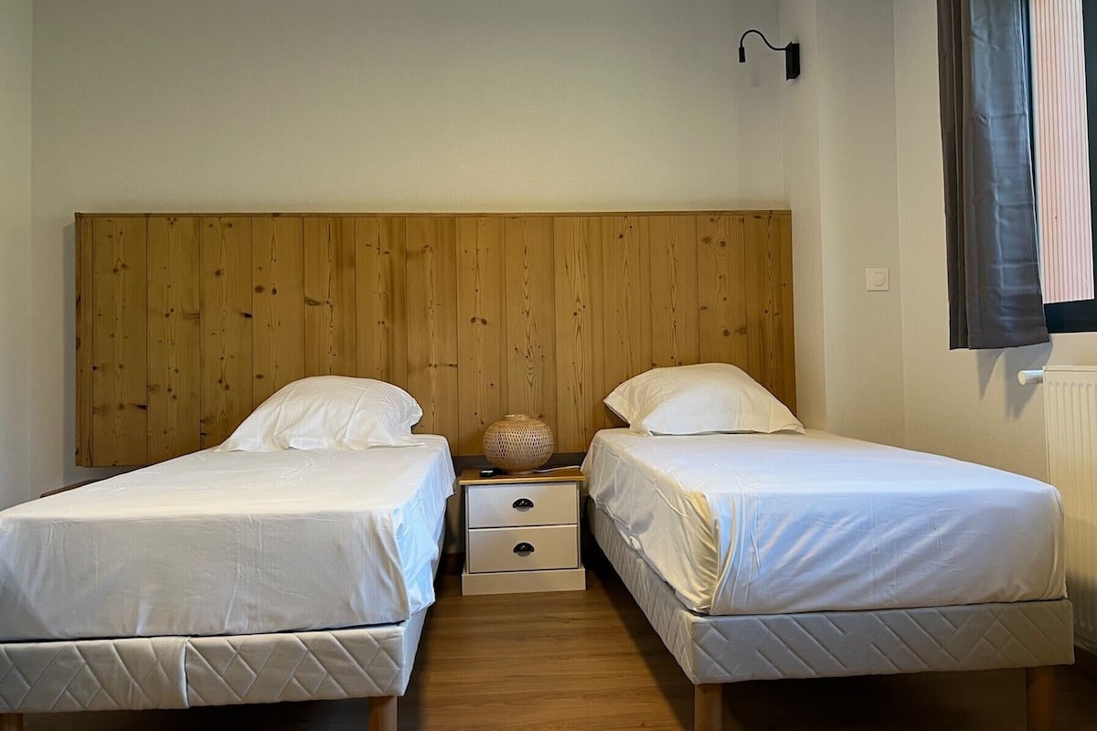 Ein Zimmer mit zwei Betten, einem Holzkopfende, Nachttischen und einer Wandlampe.