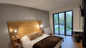 A bedroom with a large bed, wooden headboard, bedside lamps, a small bedside table, and a view of a balcony with a wooden deck.