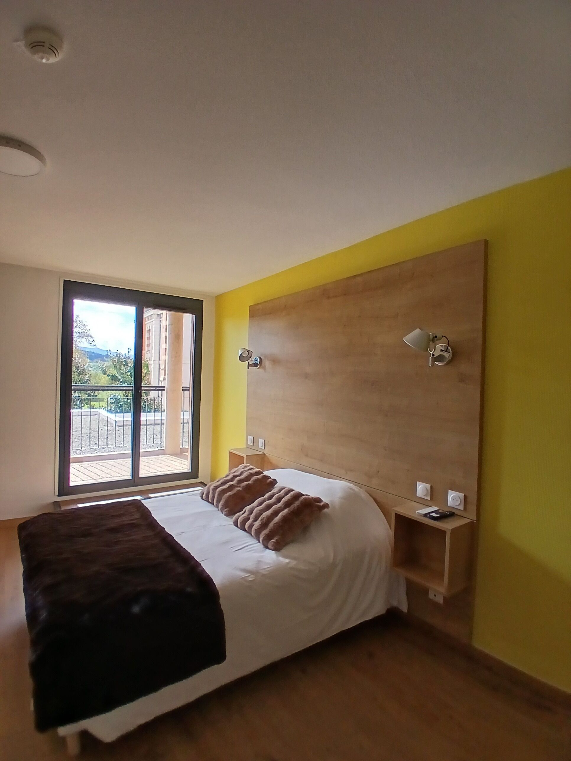 A bedroom with a large bed, a wooden headboard, and a view through a sliding glass door.
