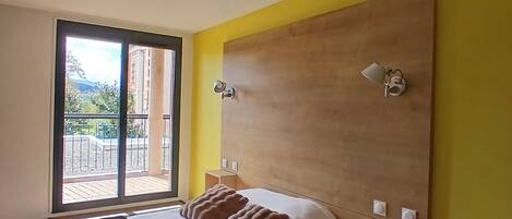 A bedroom with a large bed, a wooden headboard, and a view through a sliding glass door.