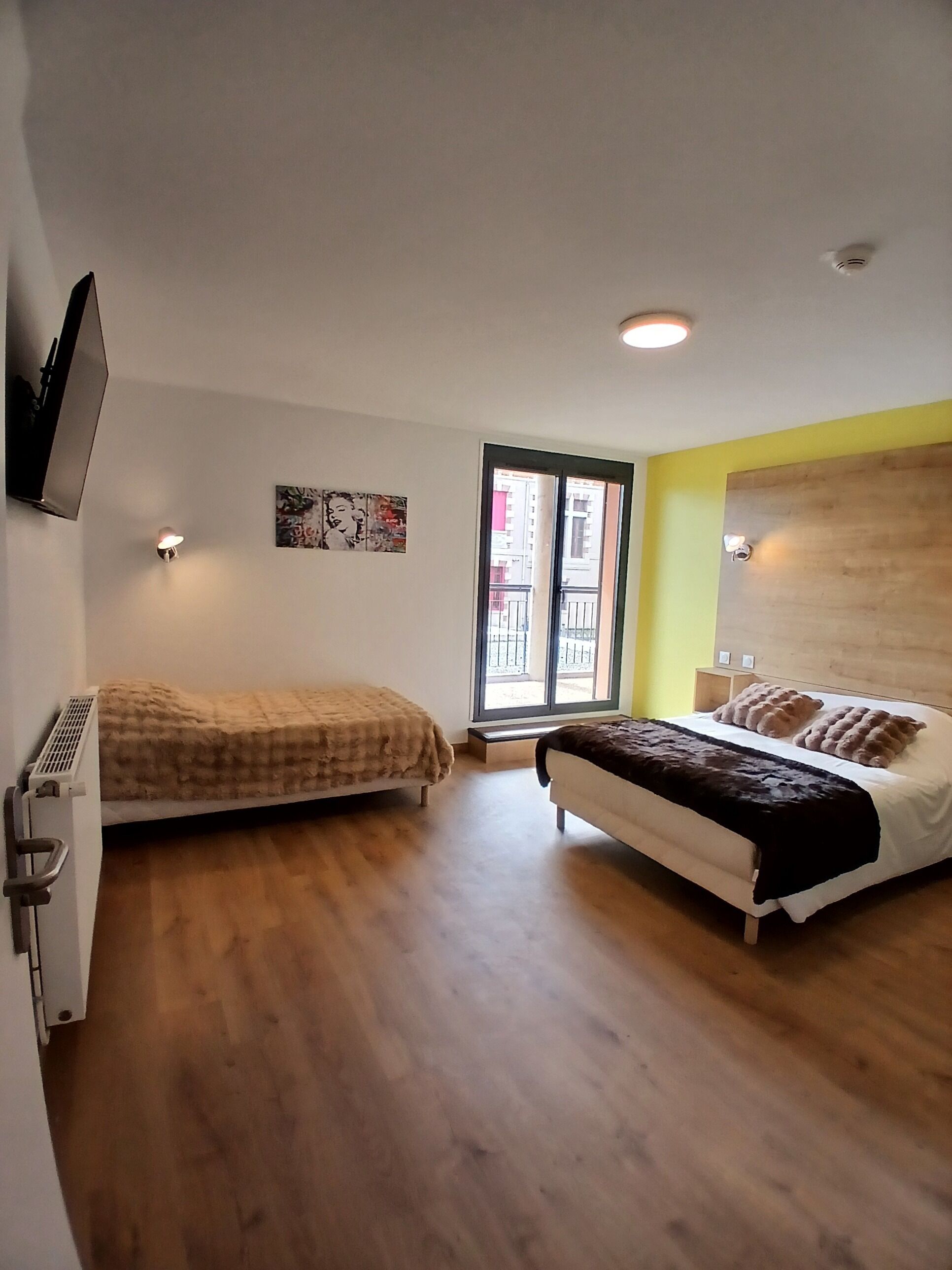 Ein Schlafzimmer mit zwei Betten, einem Fernseher und einem Fenster mit Blick auf Gebäude.