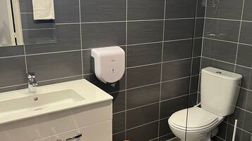A modern bathroom with a white sink, a toilet, and a hand dryer.