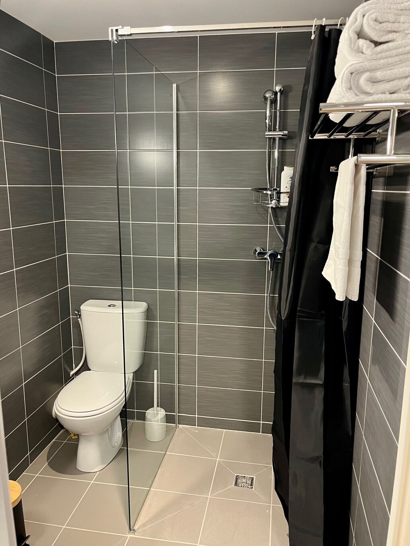 A modern bathroom with a glass shower enclosure, a toilet, and a black shower curtain.