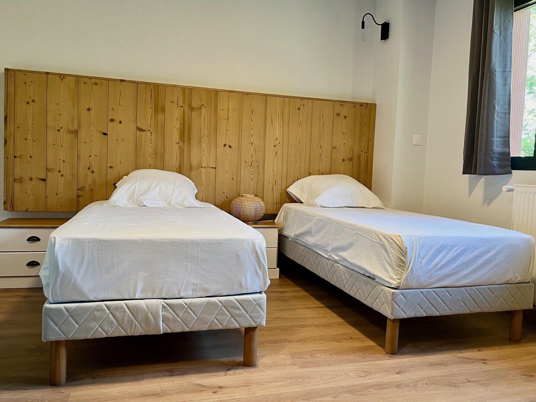 Una habitación con dos camas, cabecero de madera, ropa de cama blanca y una mesita de noche con lámpara.