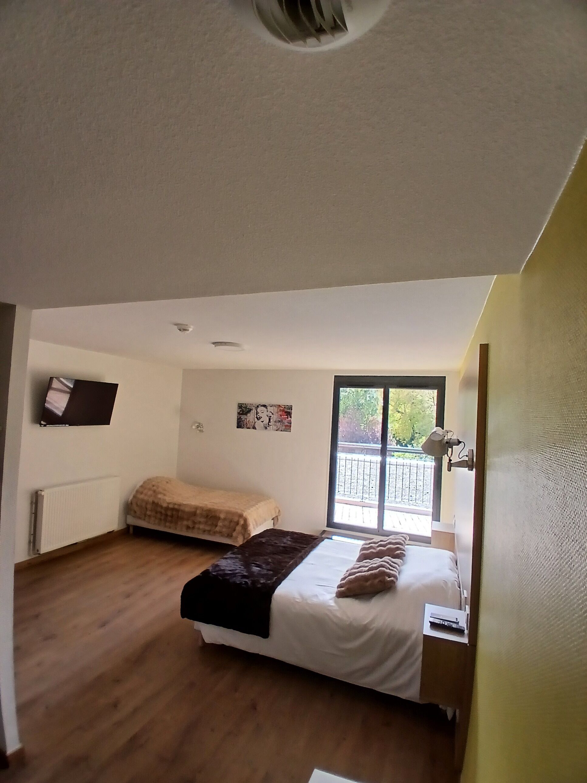 Un dormitorio con dos camas, un radiador, un respiradero en el techo, una ventana con vistas y una lámpara fijada a la pared.