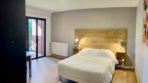 A bedroom with a large bed, a wooden headboard, a bedside table with a lamp, and a view through a glass door to an outdoor area.