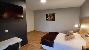A hotel room with a bed, a desk, a chair, a TV mounted on the wall, and a painting on the wall.
