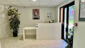 A reception area with a white desk, a large potted plant, a colorful artwork, and a map on the wall.