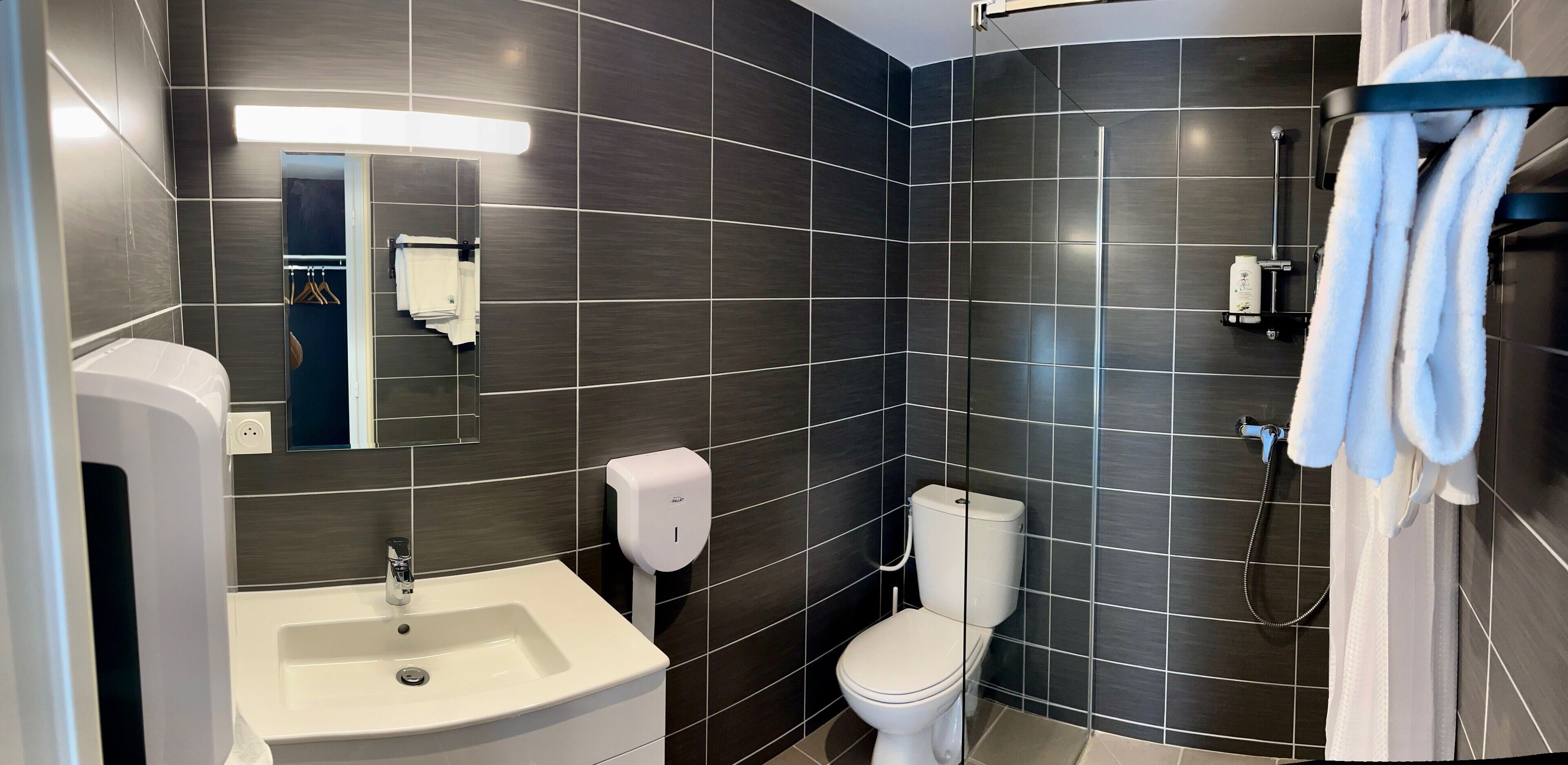 A modern bathroom with dark tiles, a white sink, a toilet, and a shower area.