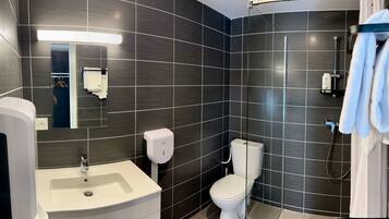 A modern bathroom with dark tiles, a white sink, a toilet, and a shower area.
