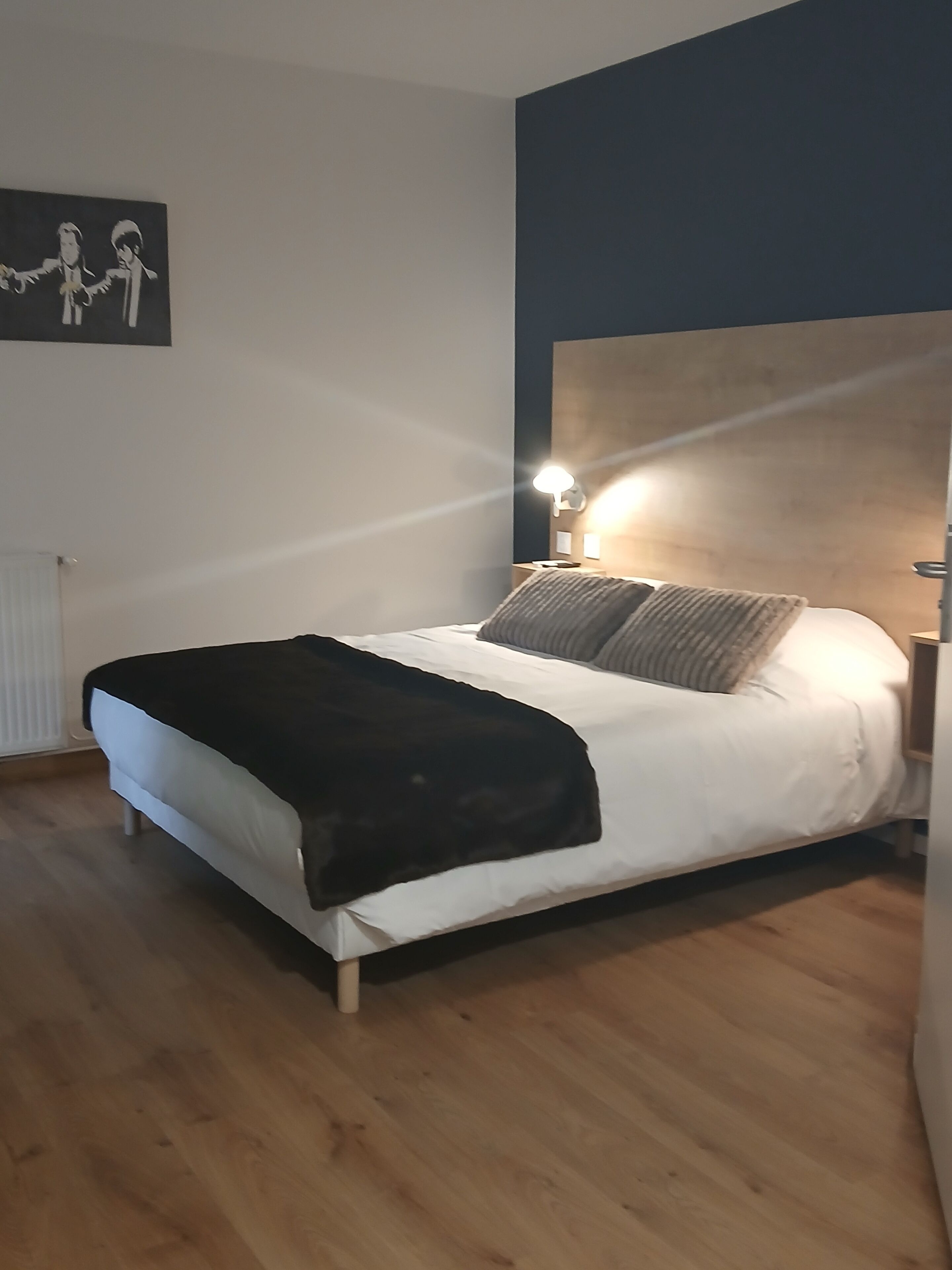 Un dormitorio con una cama, cabecera, mesita de noche y una lámpara de pared.