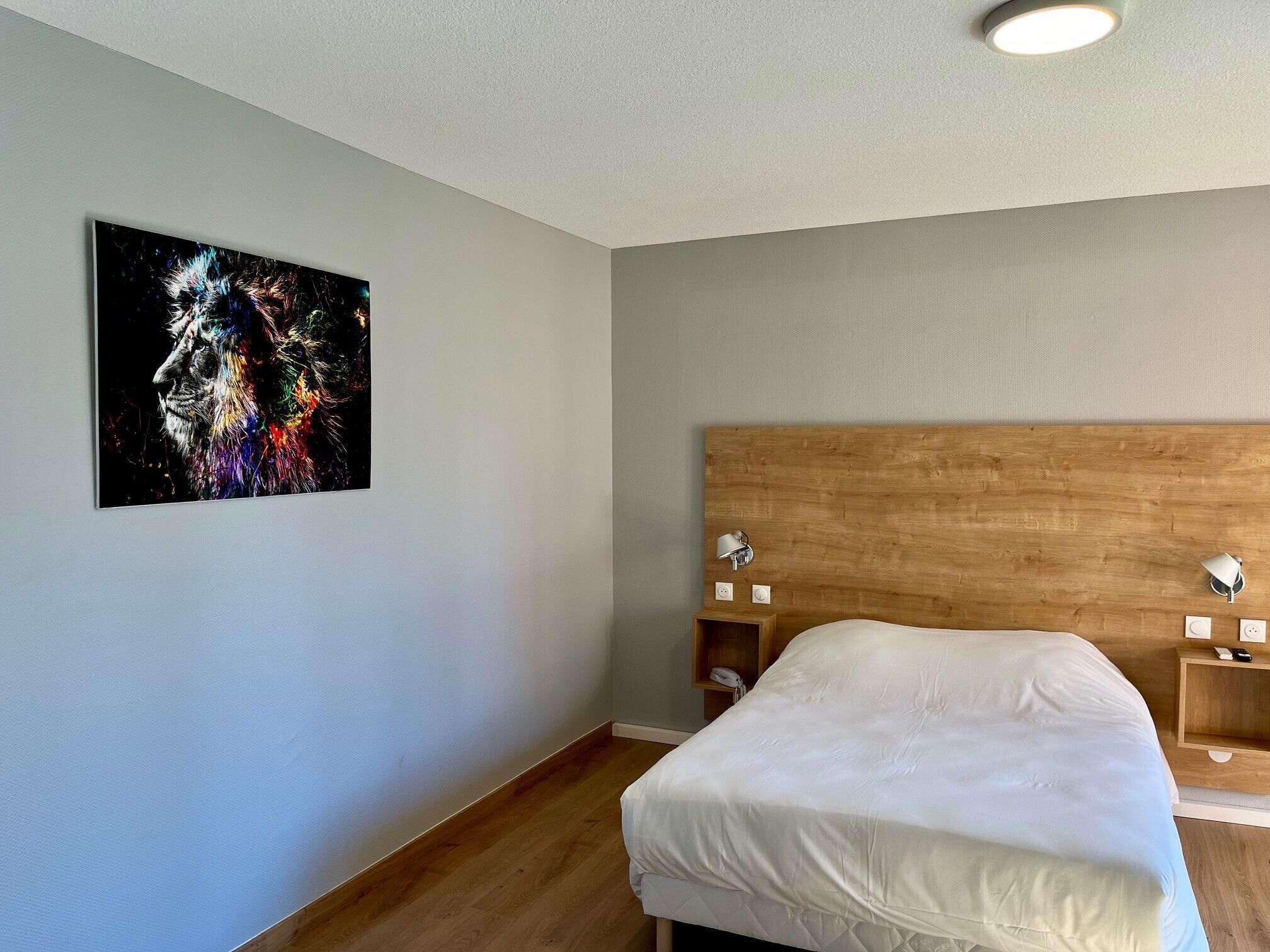 Ein Schlafzimmer mit einem Holzkopfteil, einem weißen Bett, einem Wandbild, Nachttischen mit Lampen und einer Deckenleuchte.