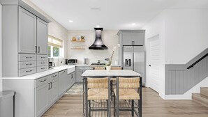 Una cocina moderna con armarios grises, encimera blanca, una isla central con sillas y una campana extractora negra.