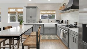Una cocina moderna con armarios grises, una estufa de acero inoxidable y un amplio ventanal con persianas.