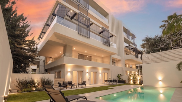 A modern multi-story building with a swimming pool, outdoor seating, and a well-lit patio area. - The Samirah Luxury Residences (Elliniko-Argyroupoli)