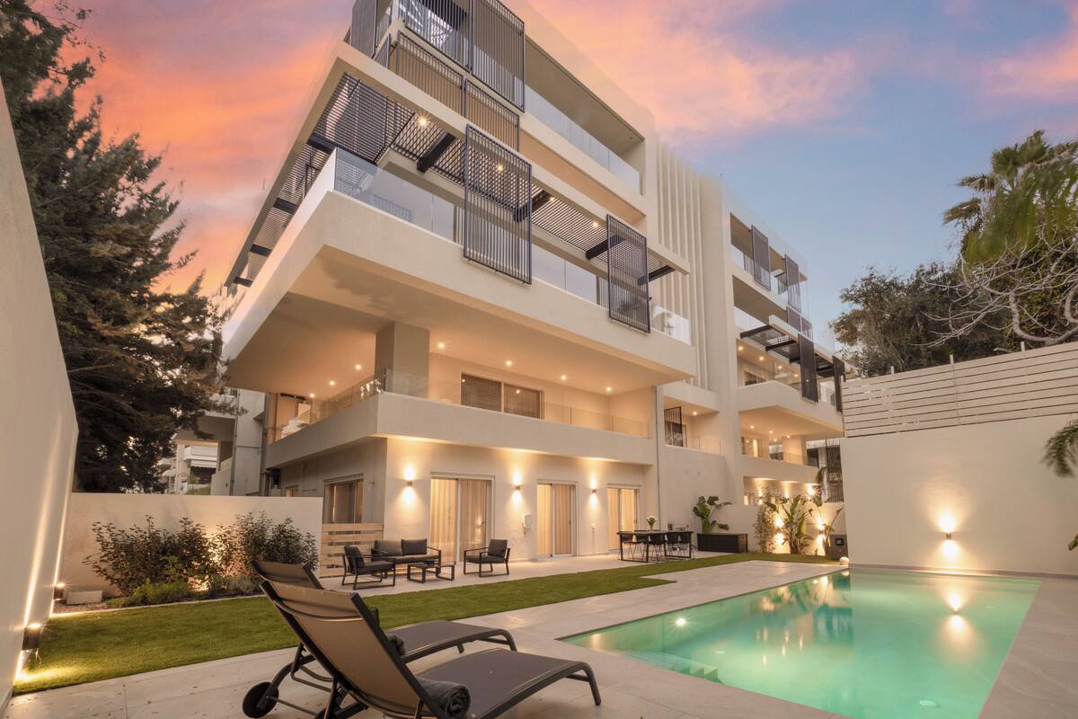 A modern multi-story building with a swimming pool, outdoor seating, and a well-lit patio area.