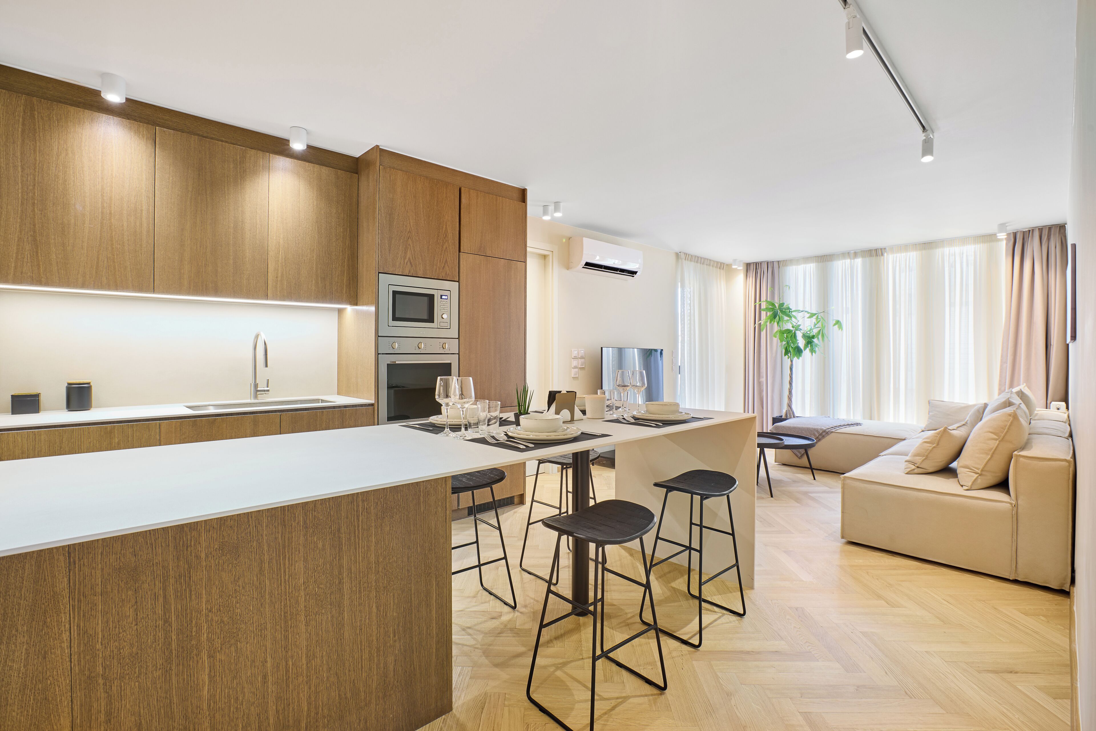 Una cocina moderna con una isla central, taburetes de bar y una zona de comedor con sofá y televisor.