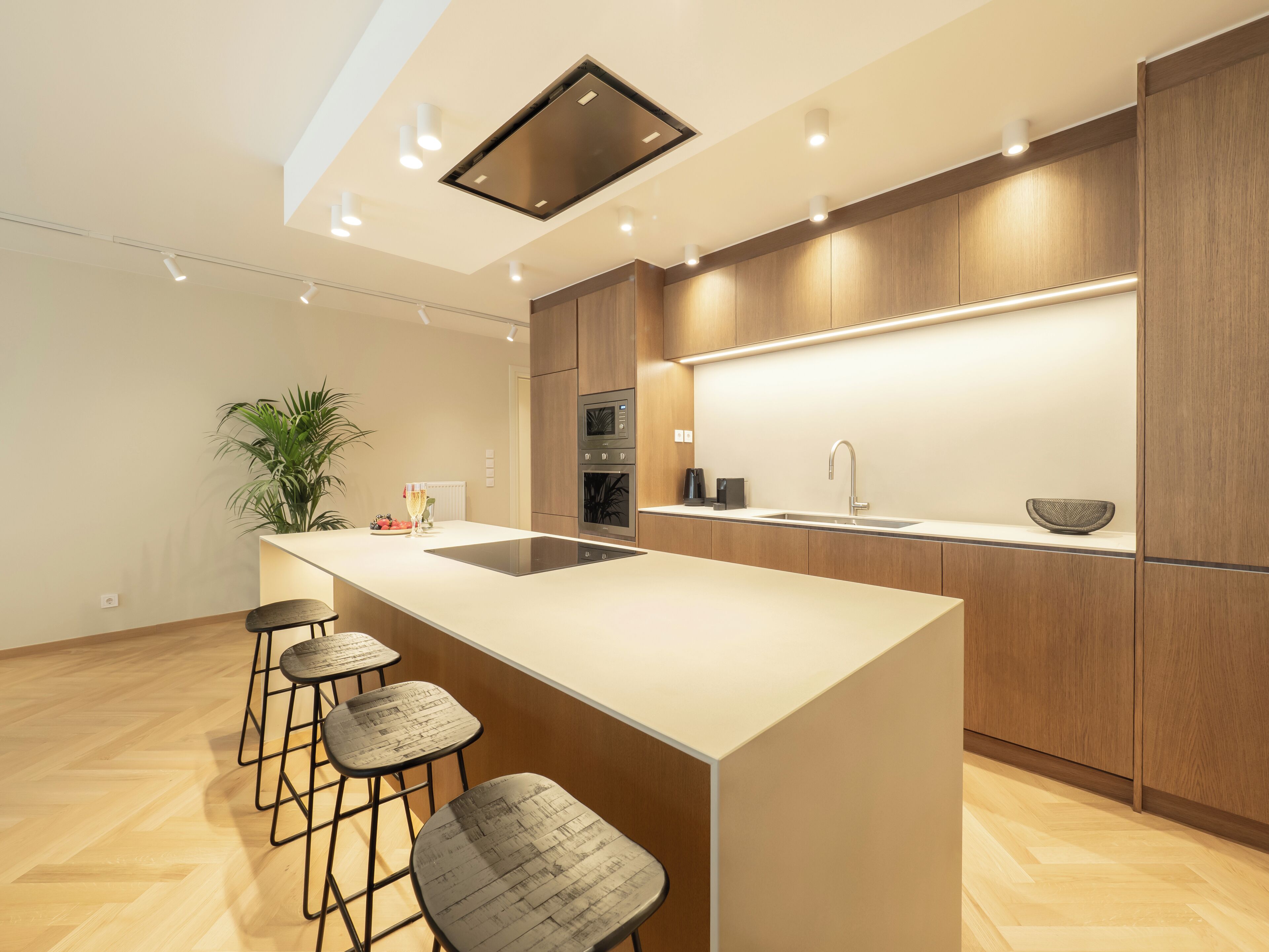 Una cocina moderna con una isla central, taburetes de bar, armarios de madera y electrodomésticos integrados.