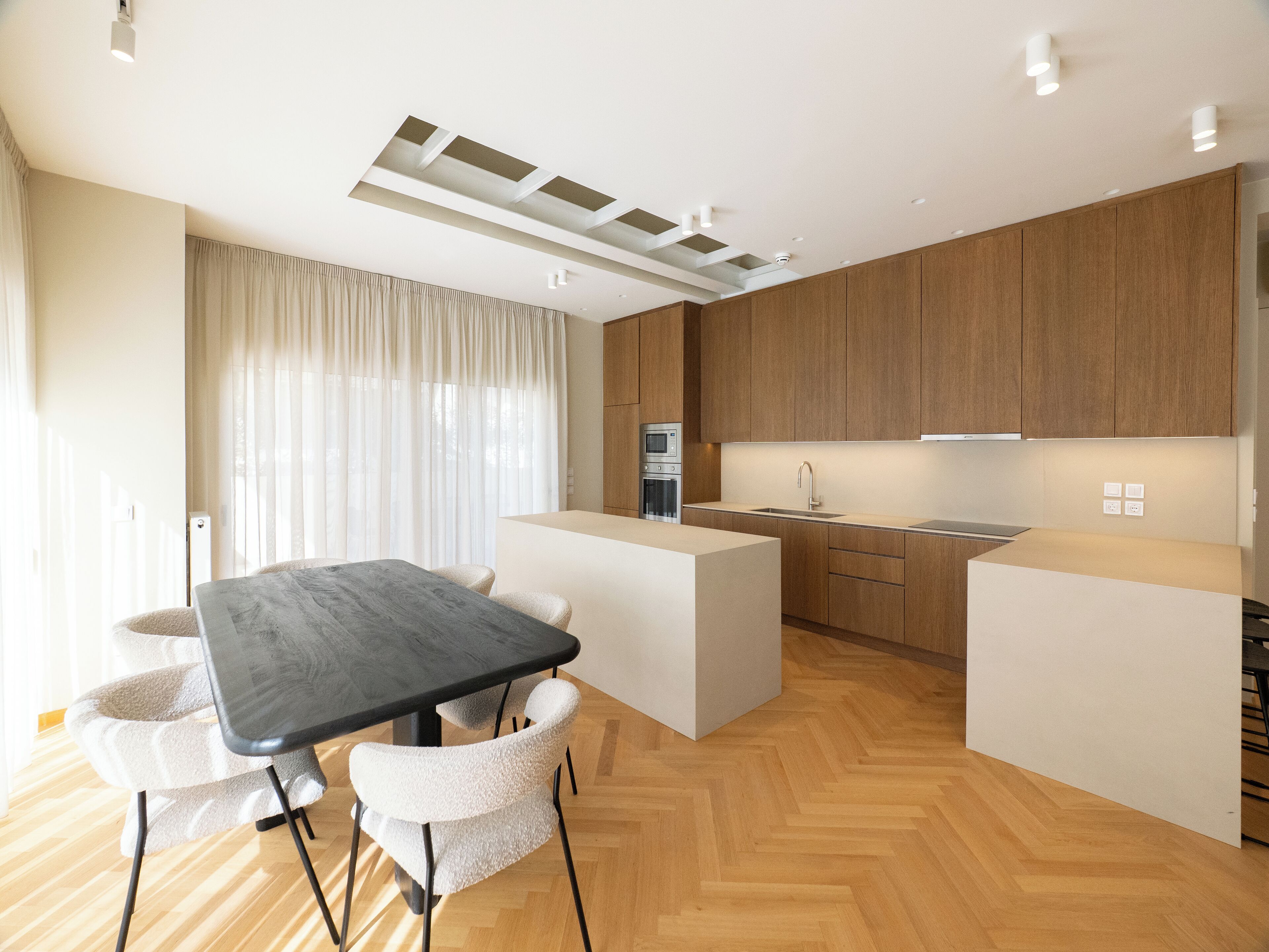 A modern kitchen with wooden cabinets, a central island, and a dining area with a table and chairs.