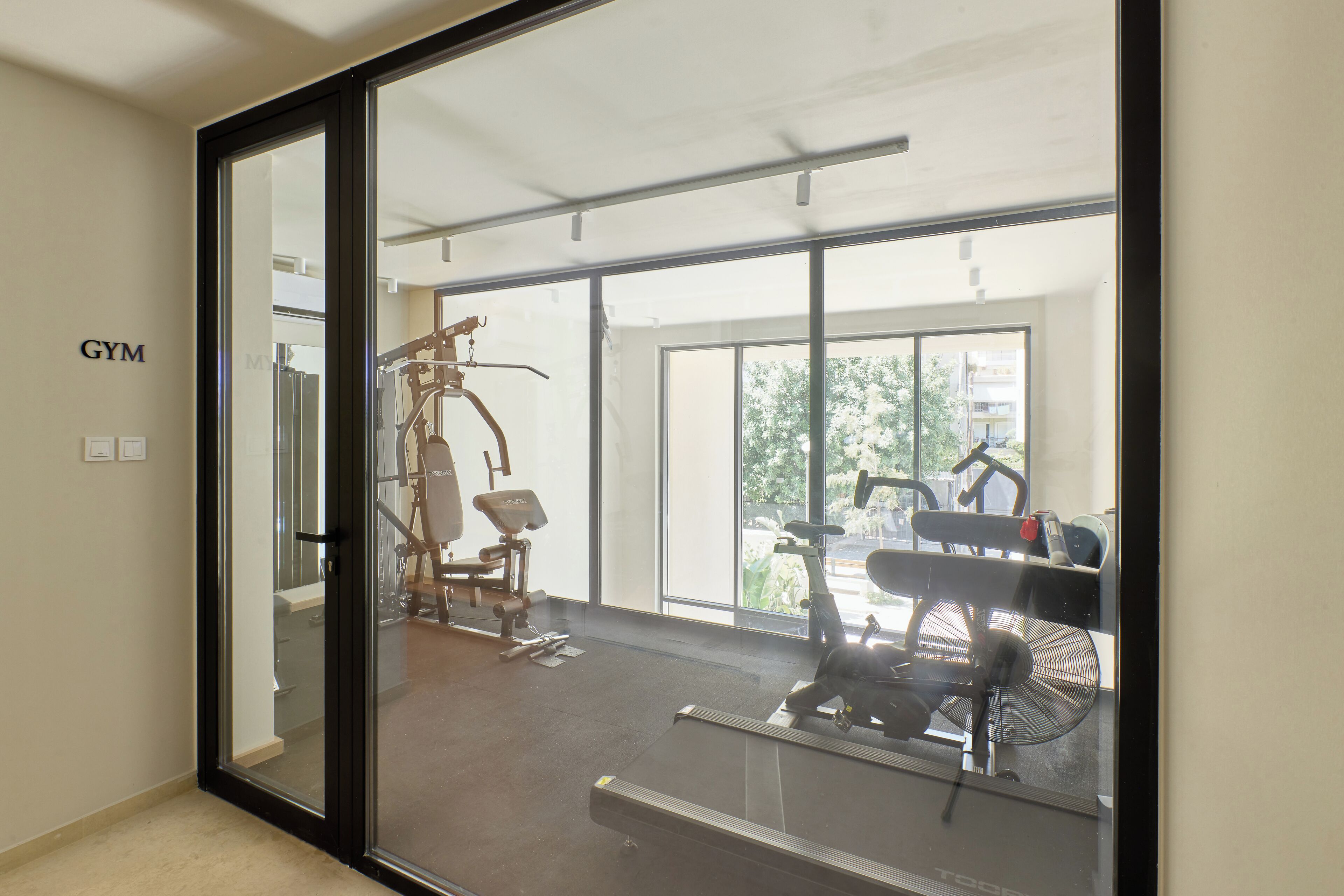 A gym with exercise equipment, large windows, and a visible outdoor view.