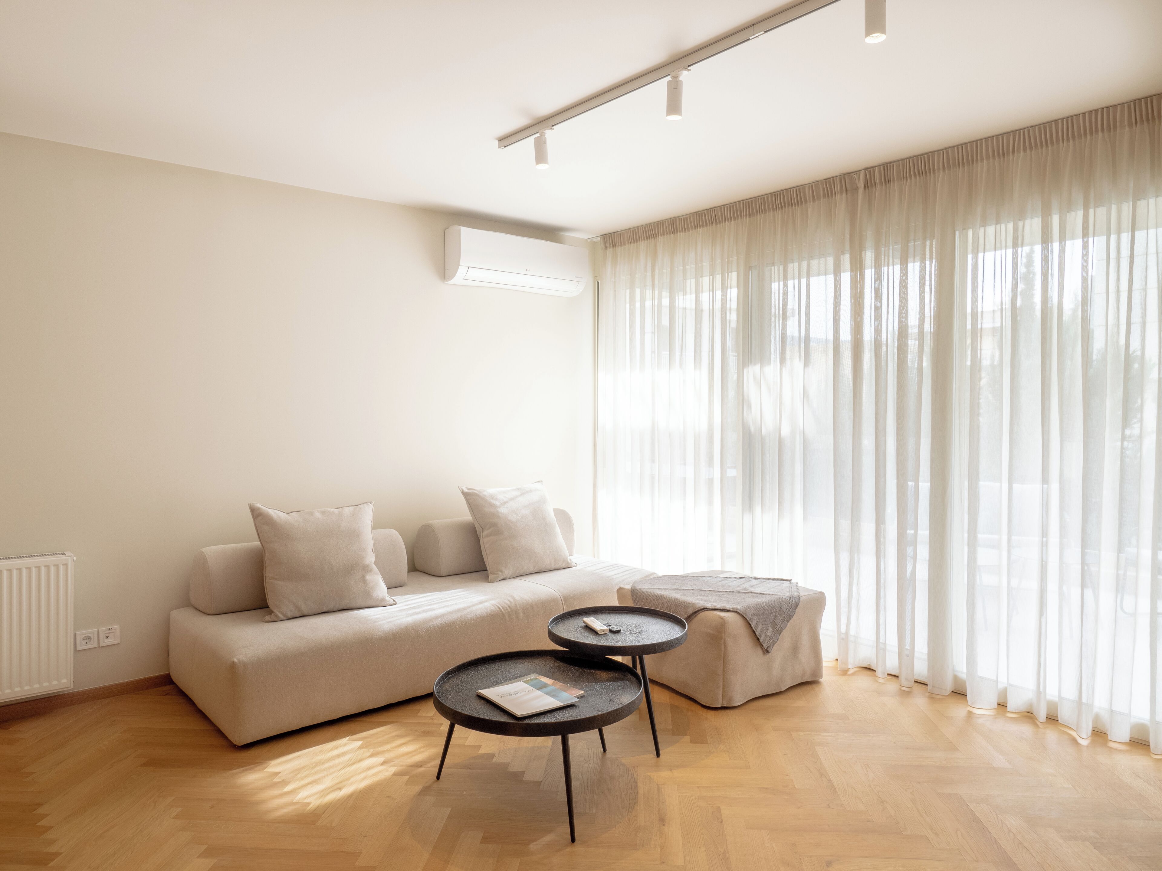 A modern living room with a sofa, two side tables, and a large window with sheer curtains.