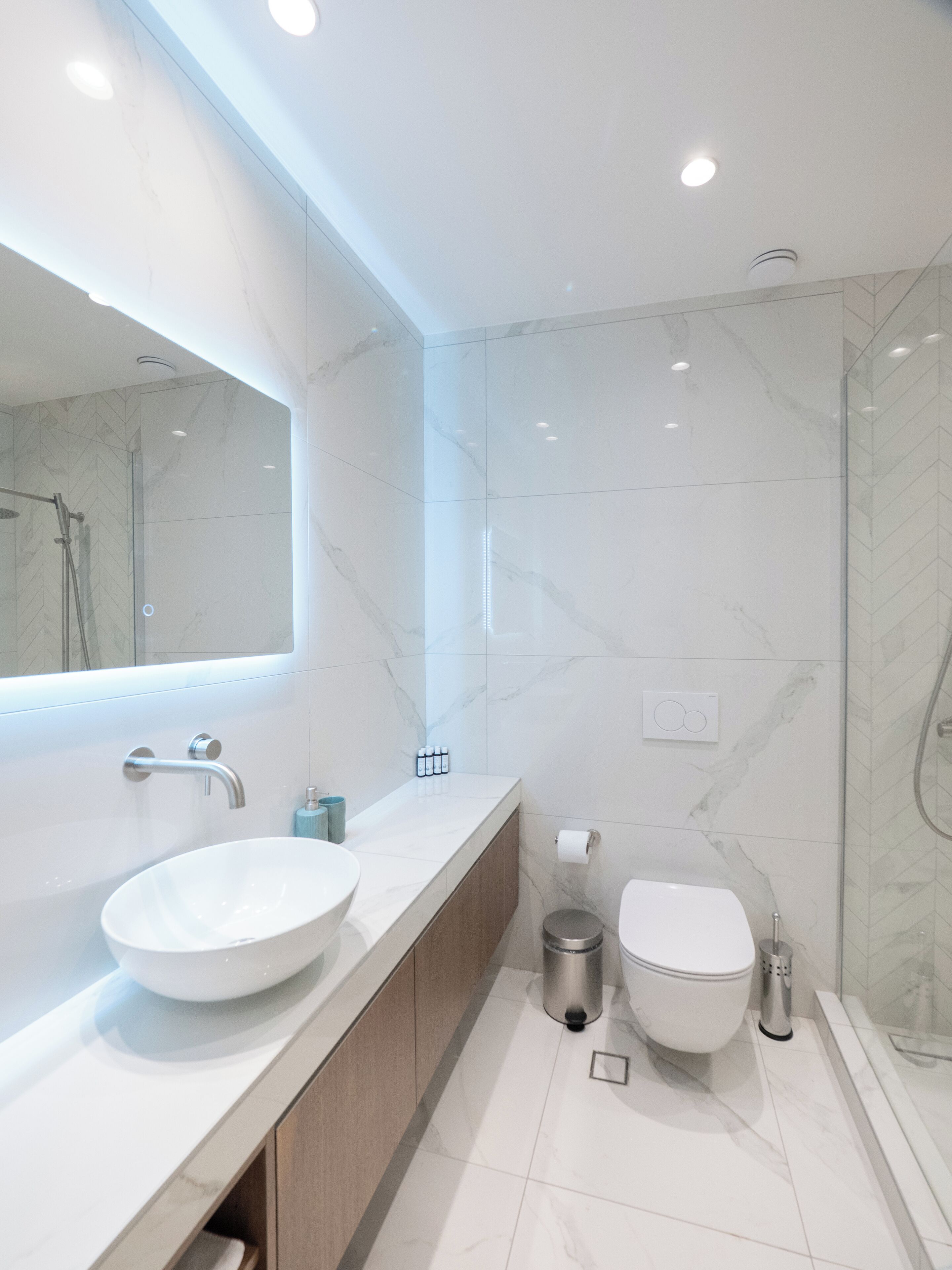 A modern bathroom with a large mirror, a vessel sink, a toilet, and a shower enclosure.