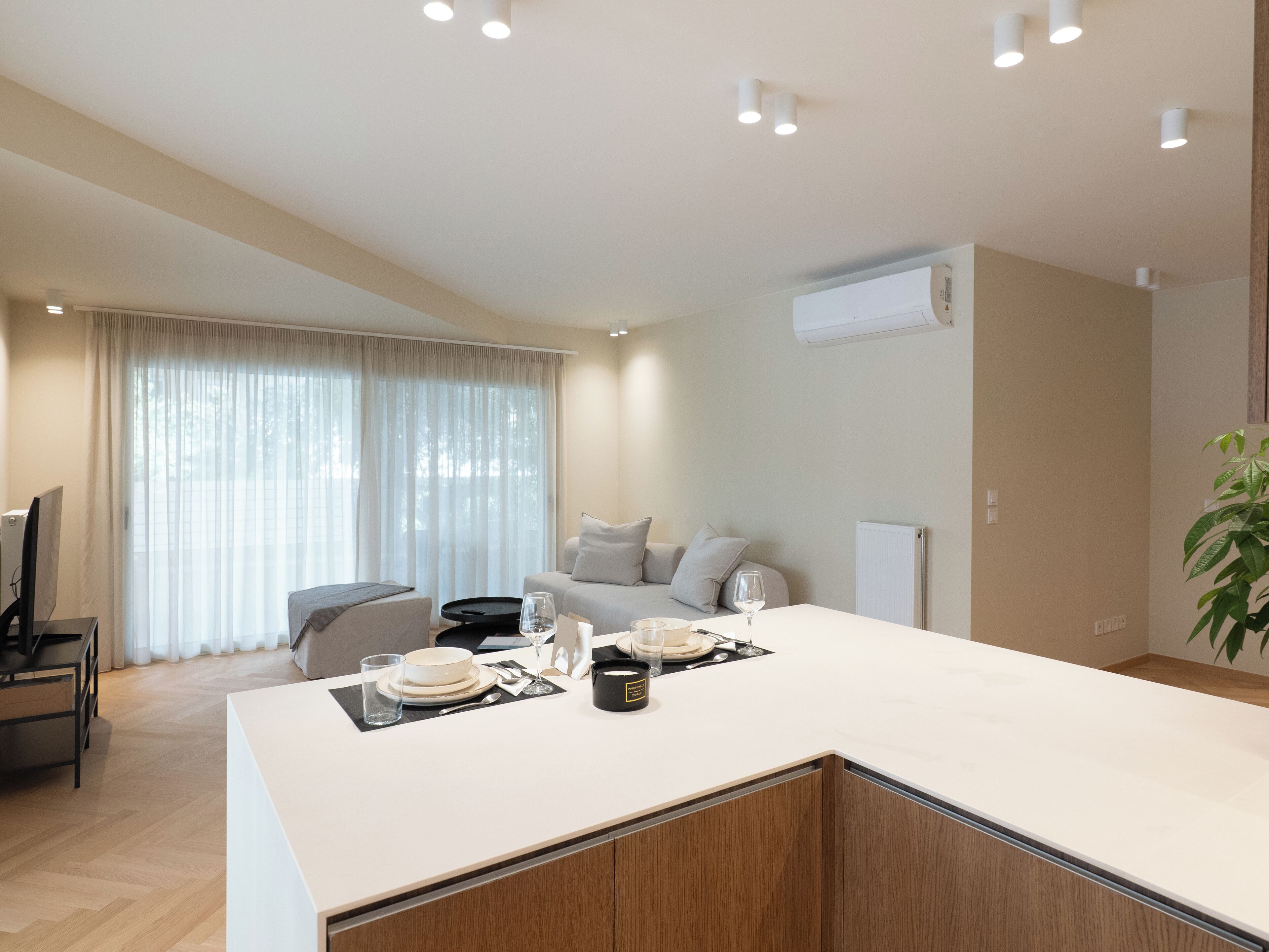 A modern kitchen with a central island, a dining area with a sofa, and a large window with sheer curtains.