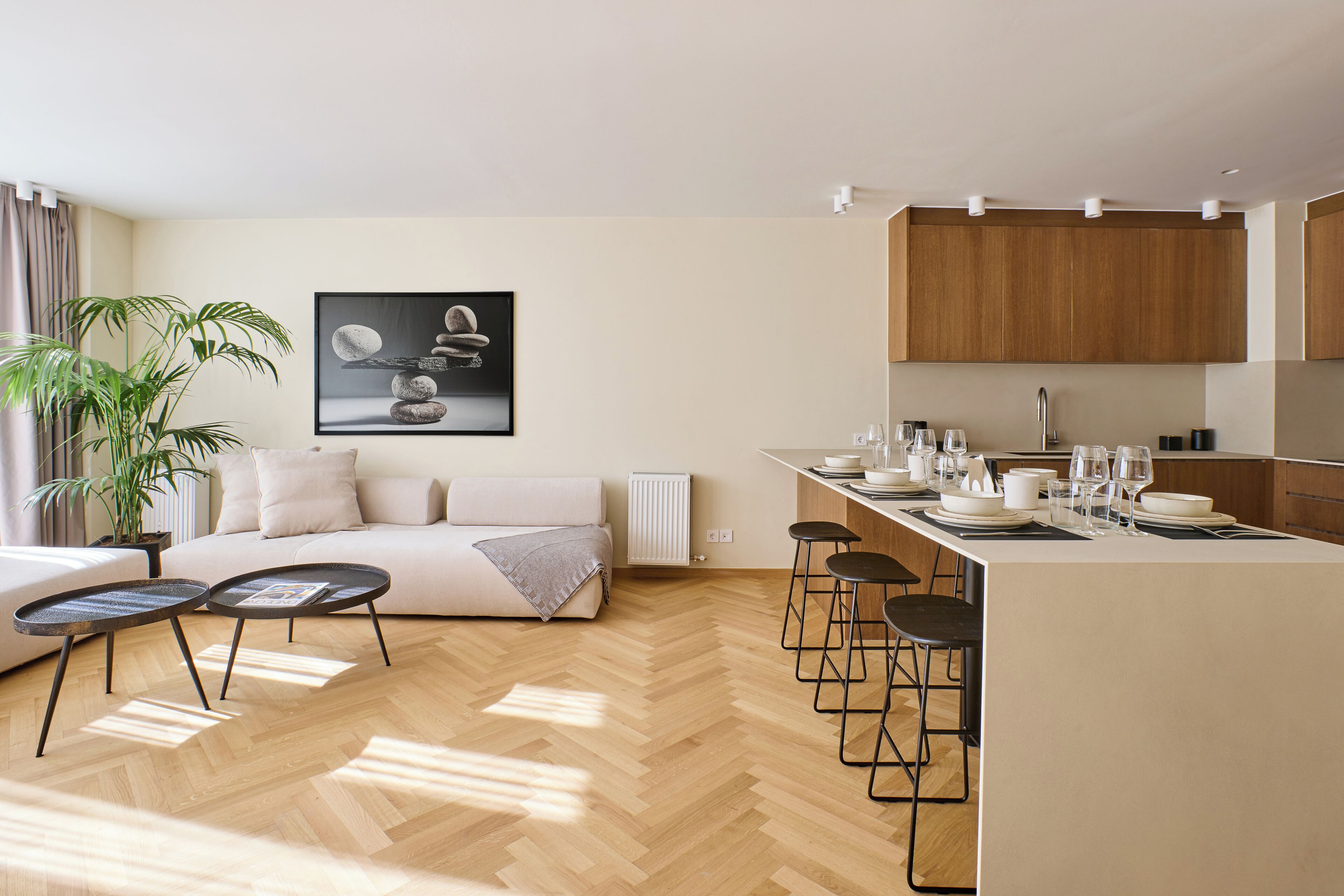 A modern living room with a sofa, two small tables, and a large potted plant. There is a kitchen area with a dining table set for four.