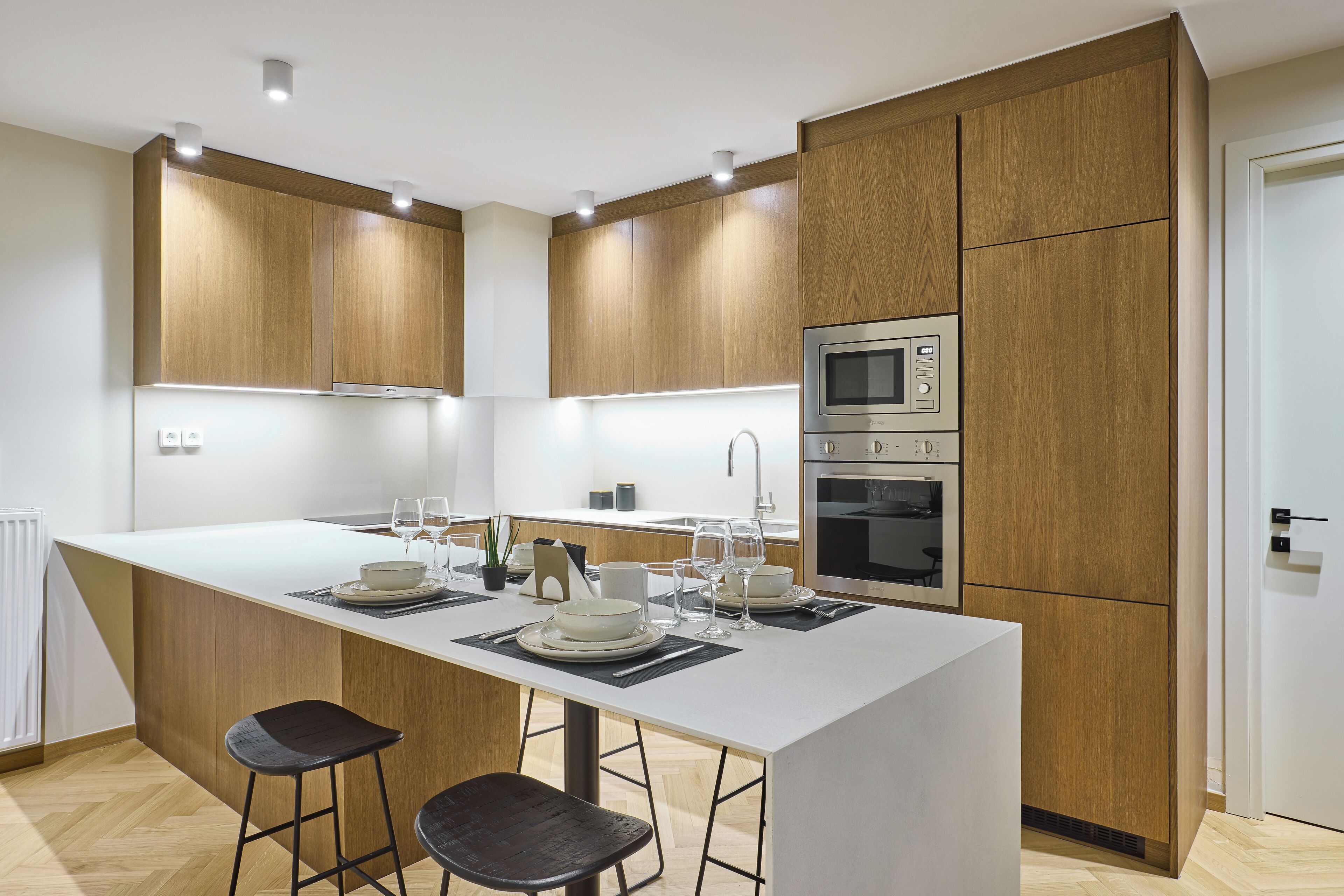Une cuisine moderne avec des meubles en bois, un îlot central doté de tabourets de bar, un four à micro-ondes encastré et un four double.