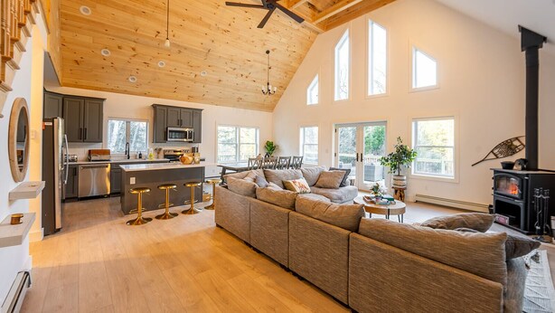 A spacious living area with a large sofa, a kitchen with modern appliances, and a fireplace. - The Perfect Modern Killington Getaway
Hot tub-Sauna-Movie Room-Speakeasy-VIEWS! (Killington)