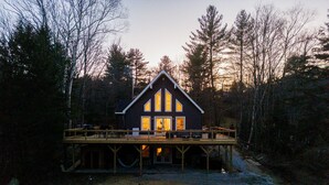 A cabin with a wooden deck, large windows, and a view of the surrounding forest. - The Perfect Modern Killington Getaway
Hot tub-Sauna-Movie Room-Speakeasy-VIEWS! (Killington)