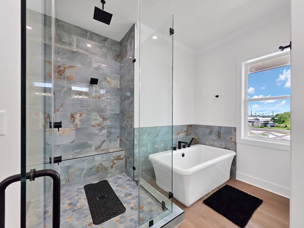 A modern bathroom with a glass-enclosed shower, a freestanding bathtub, and a view of the outside through a window.