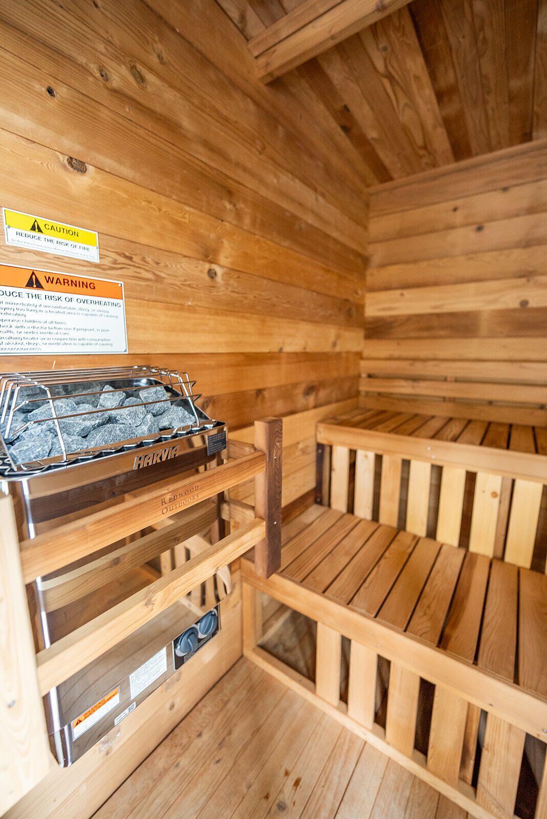 A sauna with wooden walls and benches, a metal heater, and caution and warning signs.