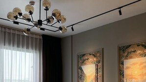 Un salon moderne avec un canapé gris, un fauteuil assorti et une table basse. Deux grandes peintures ornent le mur : l’une représente un paysage urbain et l’autre, un coucher de soleil.
