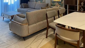 Un salon moderne avec un canapé, une table à manger et des chaises. Les murs sont ornés de tableaux et un luminaire est fixé au plafond.