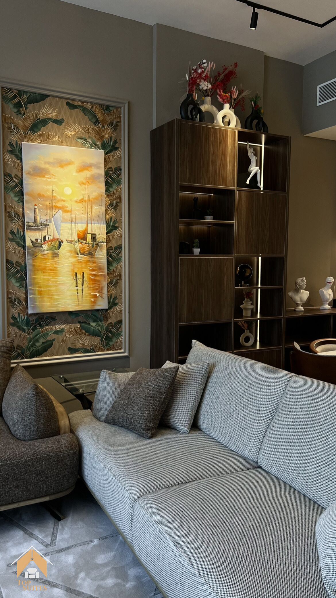 A living room with a sofa, a wooden bookshelf, and a framed painting of a seascape.