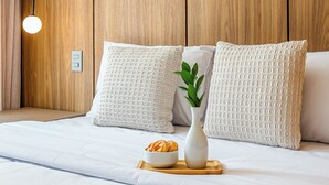 Ein ordentlich bezogenes Bett mit weißen Leinentüchern, eine kleine weiße Vase mit einer Pflanze und ein Tablett mit Gebäck.