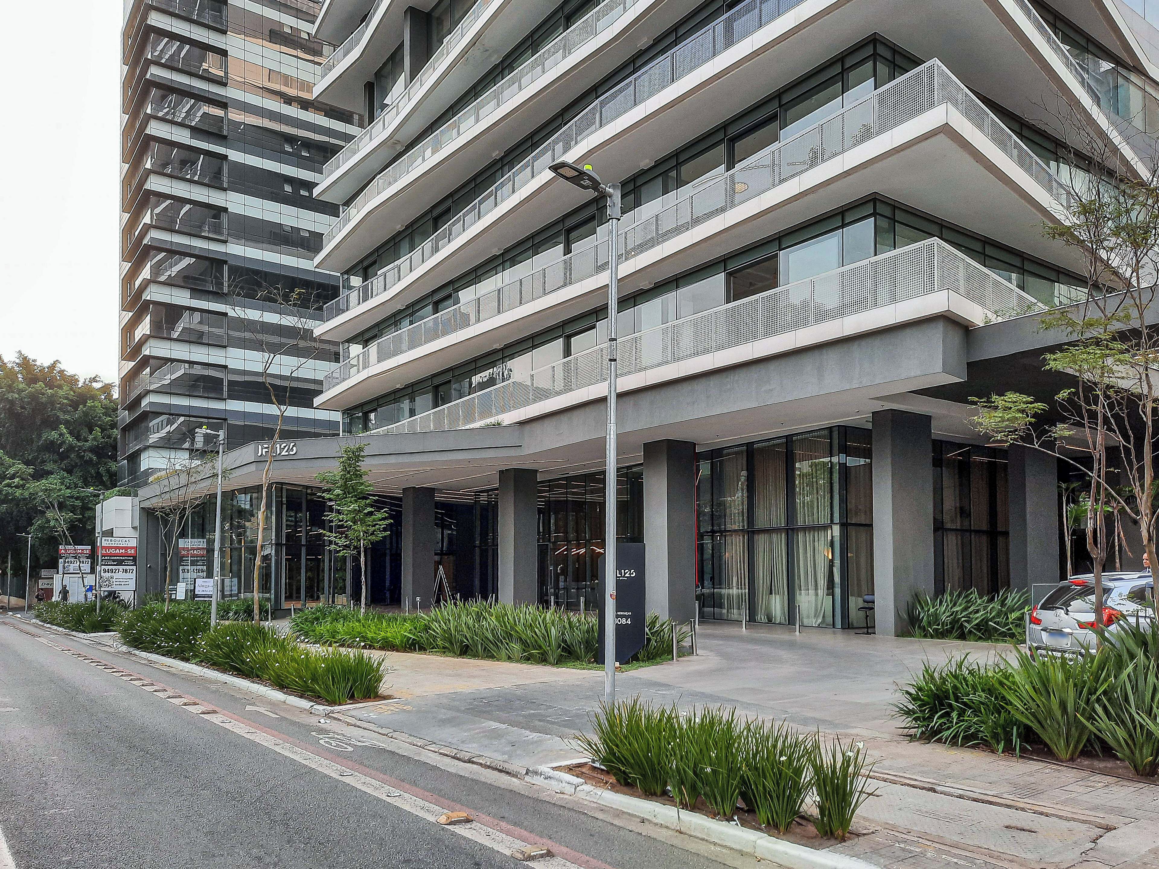 A modern multi-story building with a glass facade, outdoor seating area, and a parking lot.