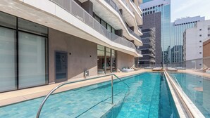 Ein Schwimmbecken mit Metallgeländer, neben einem Gebäude mit mehreren Balkonen und großen Fenstern.