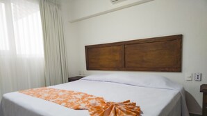 A hotel room with a large bed, white bedding, a wooden headboard, a nightstand, and a window with curtains. - Departamento Caracol (Puerto Vallarta)