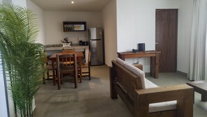 A compact living space with a dining area, a kitchenette, a wooden bench, and a ceiling fan. - Departamento Caracol (Puerto Vallarta)