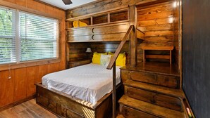 A wooden cabin-style bedroom with a bed, built-in shelves, and a staircase. - Family Friendly Cottage - Game Room+firepit+smores (Broken Bow)